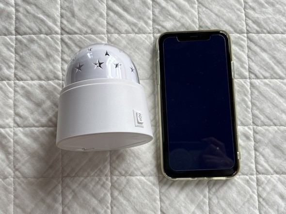 ダイソーのプラネタリウムライト(左)とiPhone 13(右)を白い布の上に並べてサイズを比較