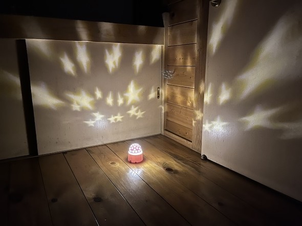暗い部屋でダイソーのプラネタリウムライトを使用し、壁や襖に多数の星形が投影されている様子