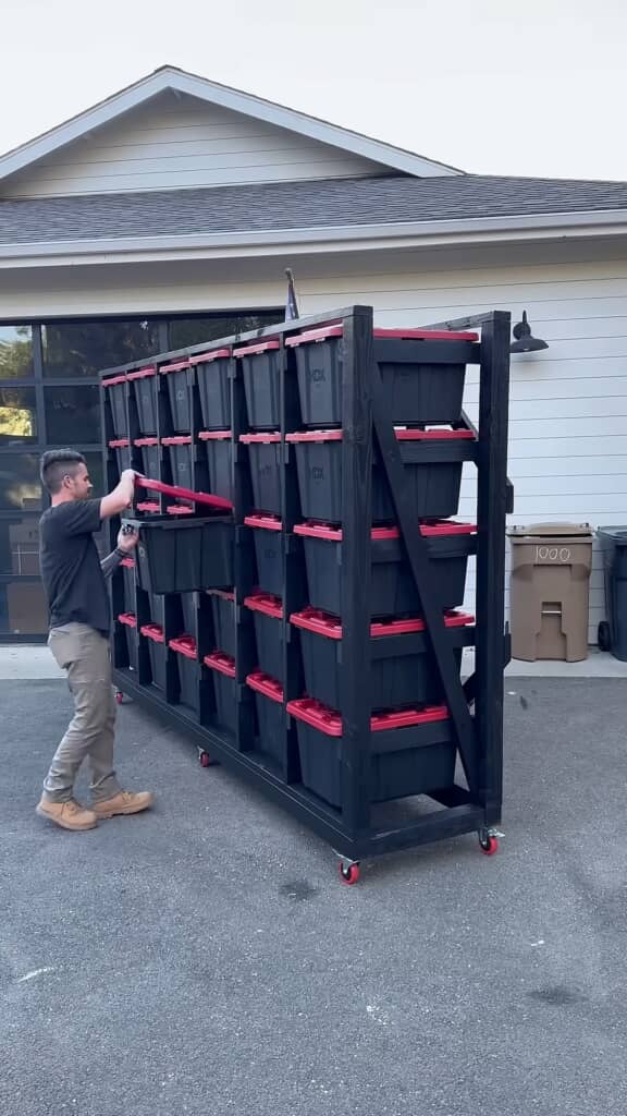 黒い木製フレームに赤いフタ付きの黒い収納ボックスが複数収納されたDIYツールラック。キャスター付きで移動可能。作業中の男性がボックスの一つを引き出している。