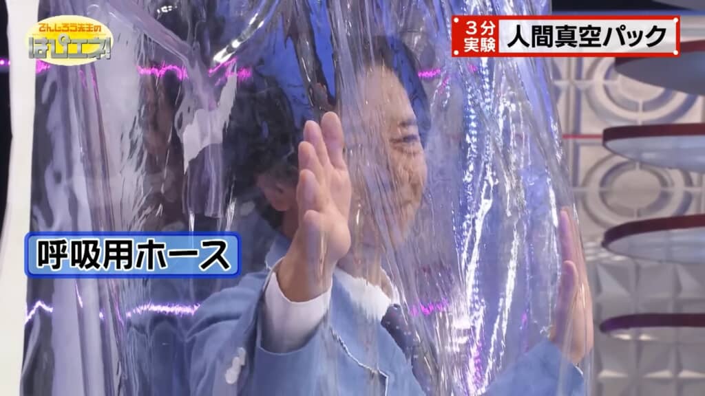 真空状態のビニール袋の中にいる男性が手を前に出して押し返すようにしている様子。袋の外から「呼吸用ホース」と書かれた青いテロップが表示されている。