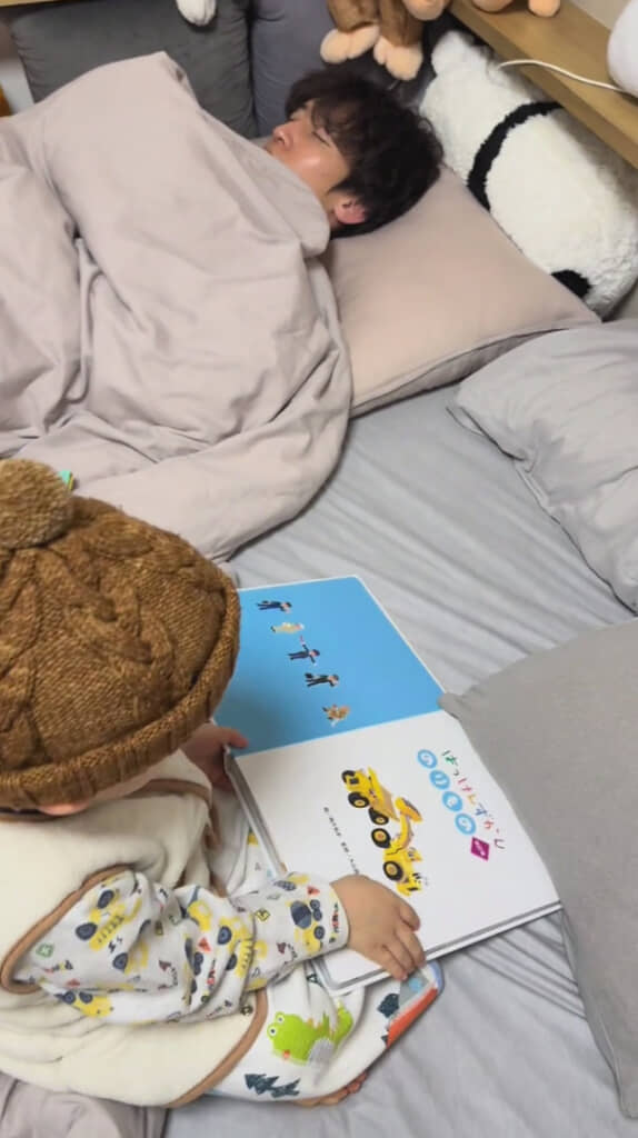 眠るパパさんの横で読書にいそしむ