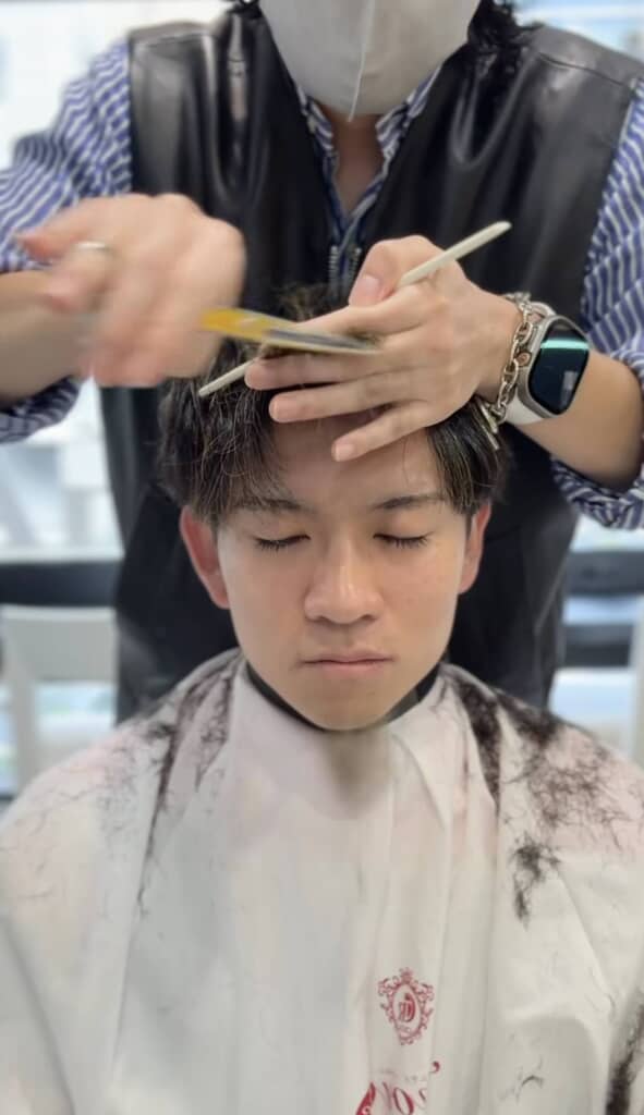 目を閉じた男性が髪を切られている