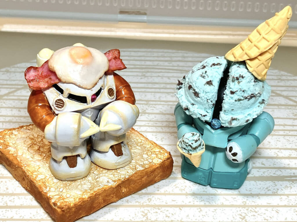 パンとベーコンエッグに挟まれて朝食風になったズゴック（左）と、頭がチョコミントアイスになったアッガイ（右）