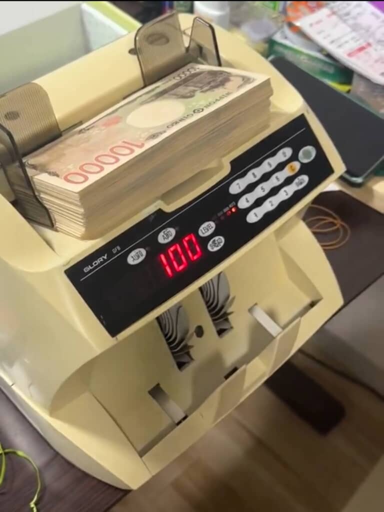 日本円の1万円札をセットした紙幣計数機、枚数「100」と表示。