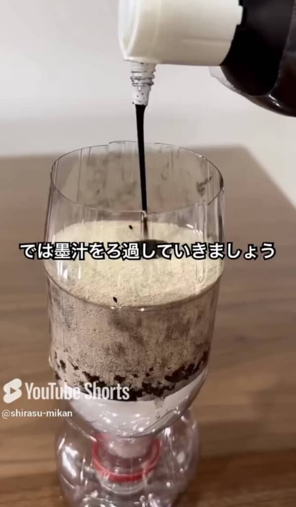 砂を詰めた自作フィルターに黒い墨汁を注ぐシーン