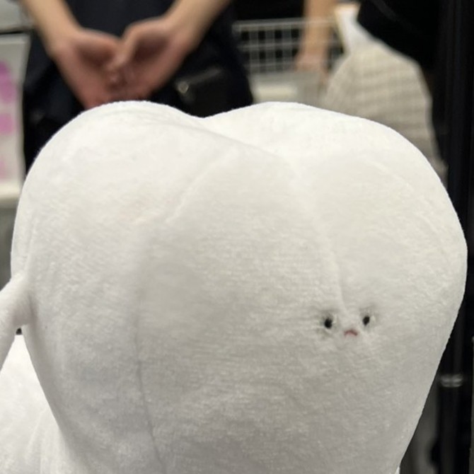 白くて歯の形をしたぬいぐるみのクローズアップ。顔が中央に小さく刺繍されている。