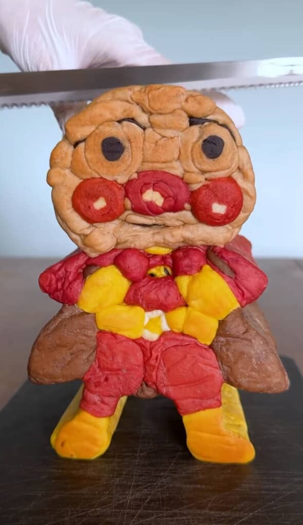 アンパンマンを模した立体的なパンの塊をナイフでカットしようとしている場面