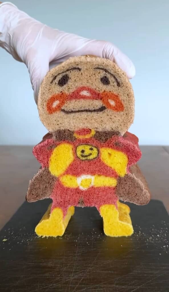 カットされた断面がアンパンマンの顔と体になっているパンを手で持ち上げている