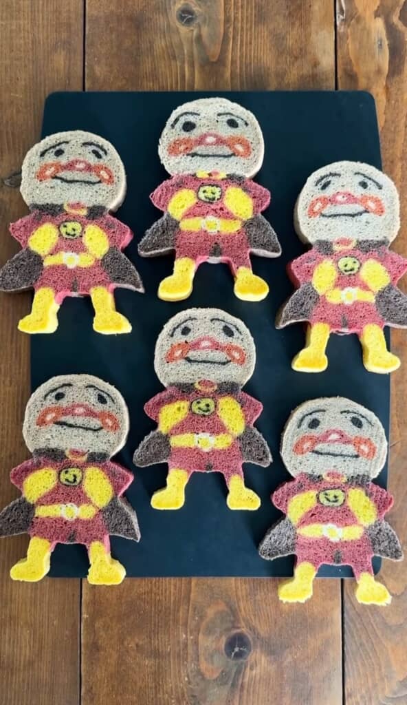 アンパンマンのキャラクター型にカットされたカラフルなパンが黒いボードの上に並べられている