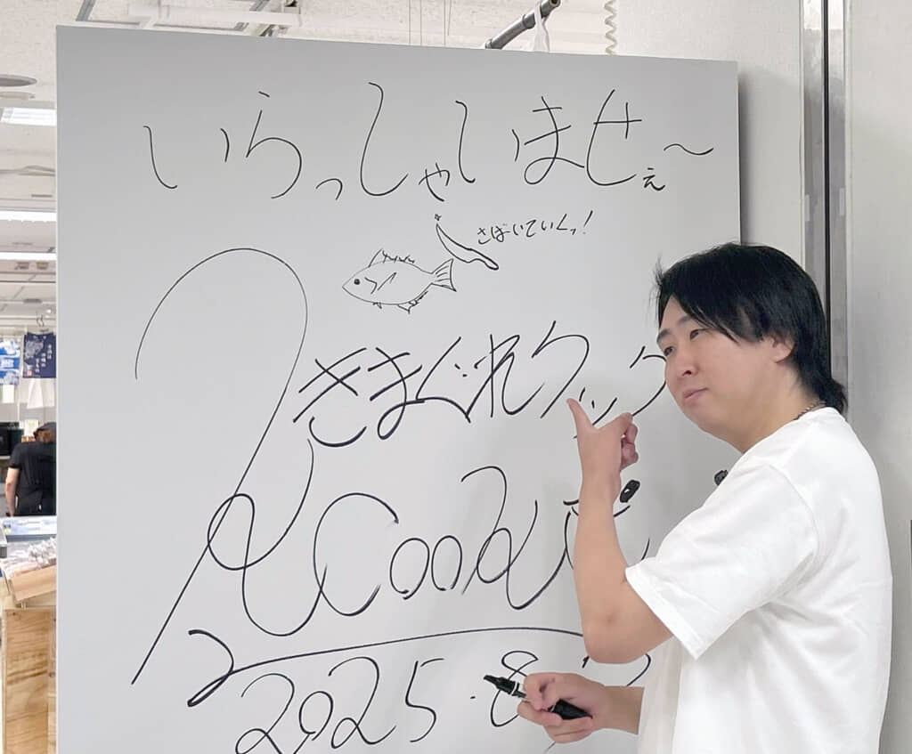その場で書いたサインを前にポーズを取るかねこさん