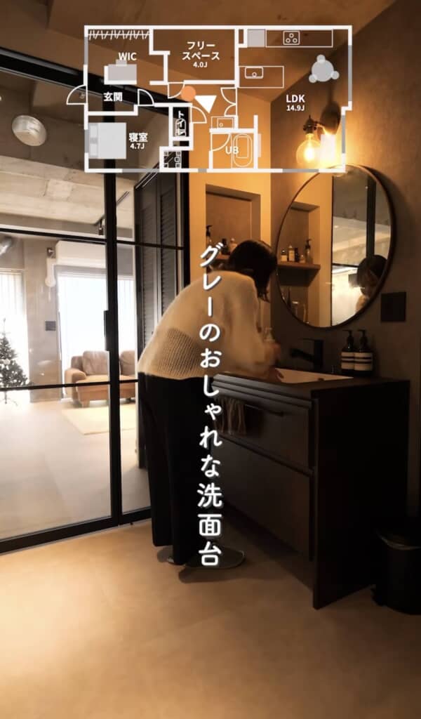 黒の洗面キャビネットと丸型ミラーがグレーの壁と調和した洗練された洗面所。