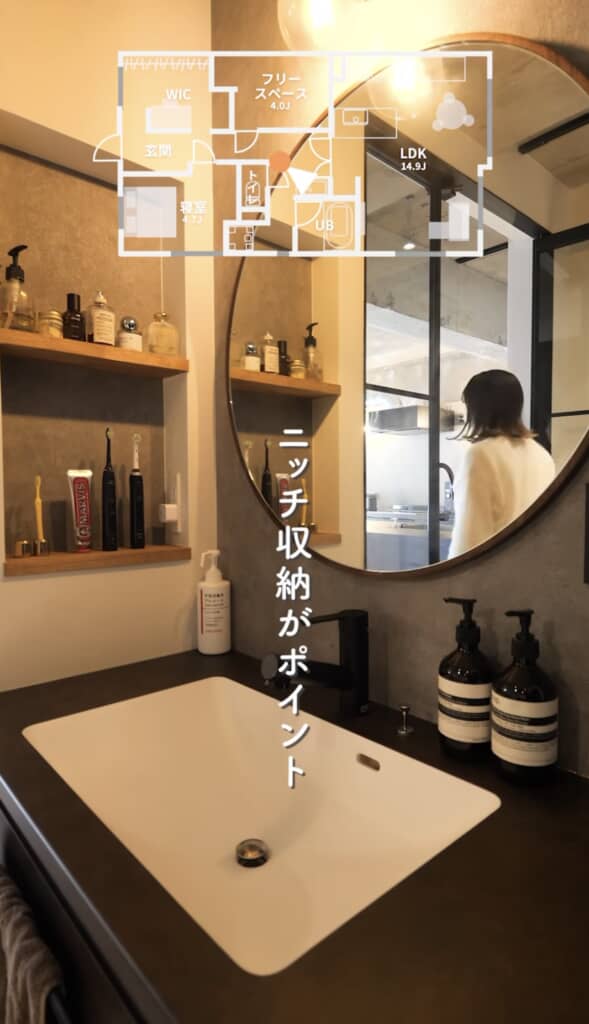 洗練された洗面所に設けられたニッチ収納と丸型ミラーが特徴的で、奥にはキッチンへ向かう女性の姿が映っている。