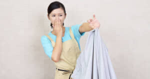 悪臭を放つ洗濯物をつまみ鼻をつまむ女性の画像