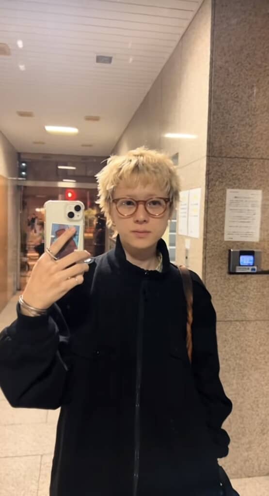 金髪メガネの男性が鏡越しに自撮りをしている