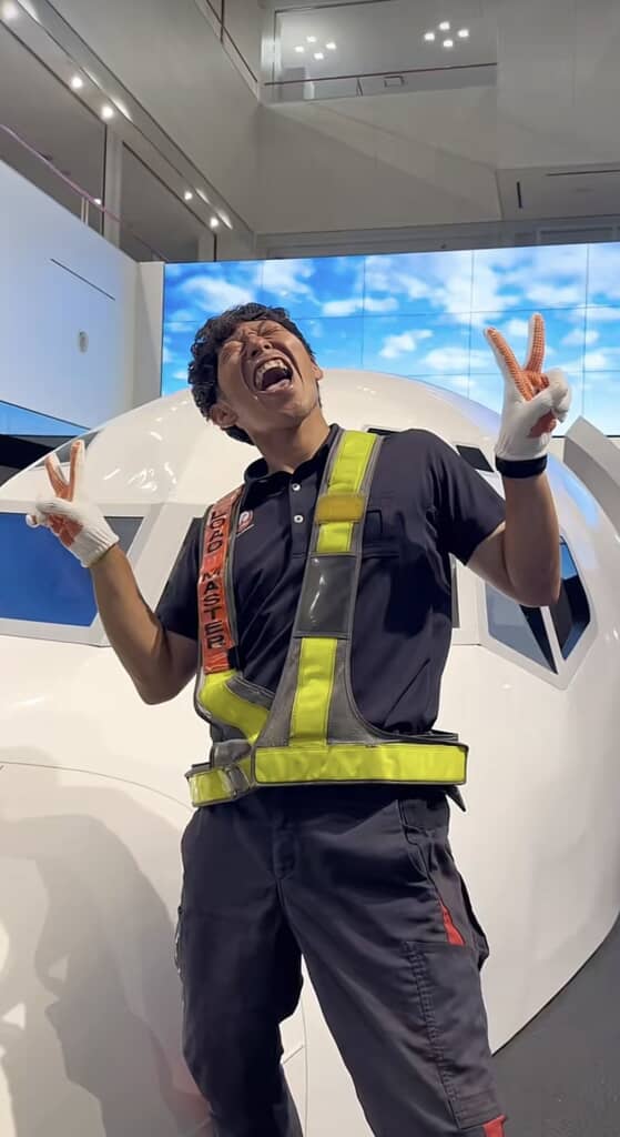 飛行機の模型の前でポーズを決める、作業服を着た男性