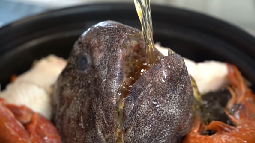 オオカミウオの口から水炊きのツユを鍋へ注ぎ込む様子