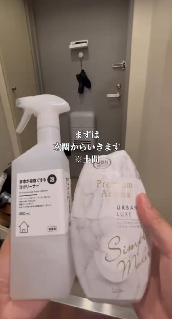 玄関のドア前で、泡クリーナーと芳香剤を両手に持つ人物の手元