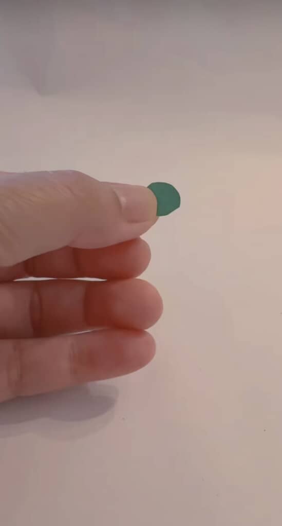 小さな緑色の紙片を指先でつまんでいる様子。
