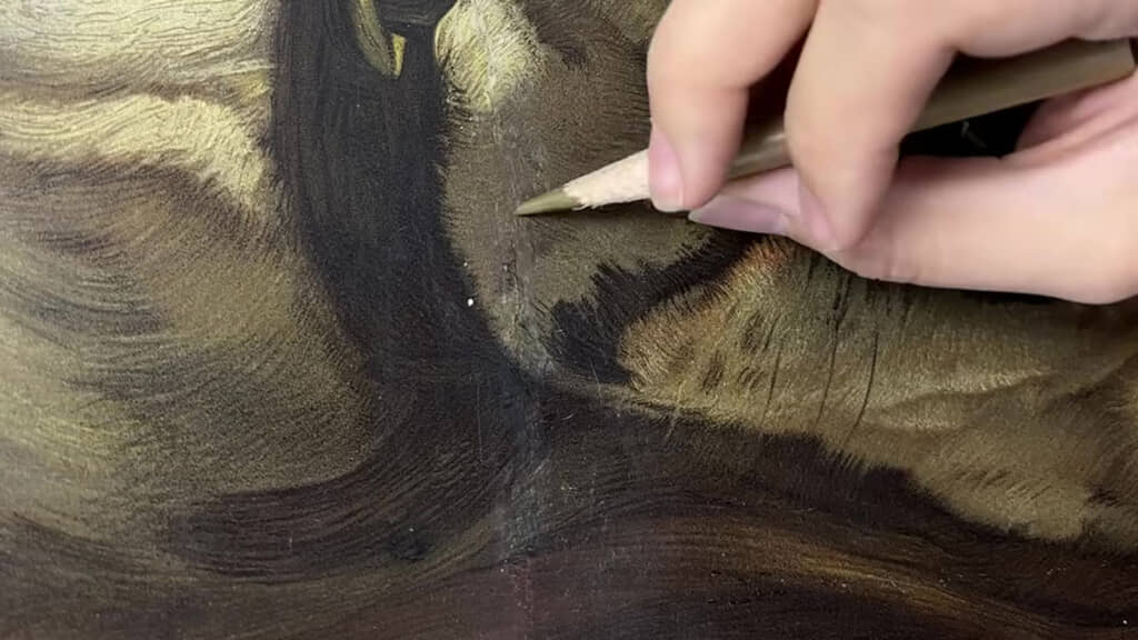 色鉛筆を使い、犬の絵の破れた部分を細かく補色している様子のアップ