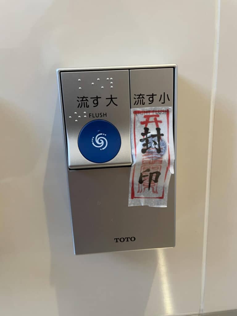 TOTO製トイレの「大」と「小」流しボタン。小ボタンには「封」のお札が貼られている。