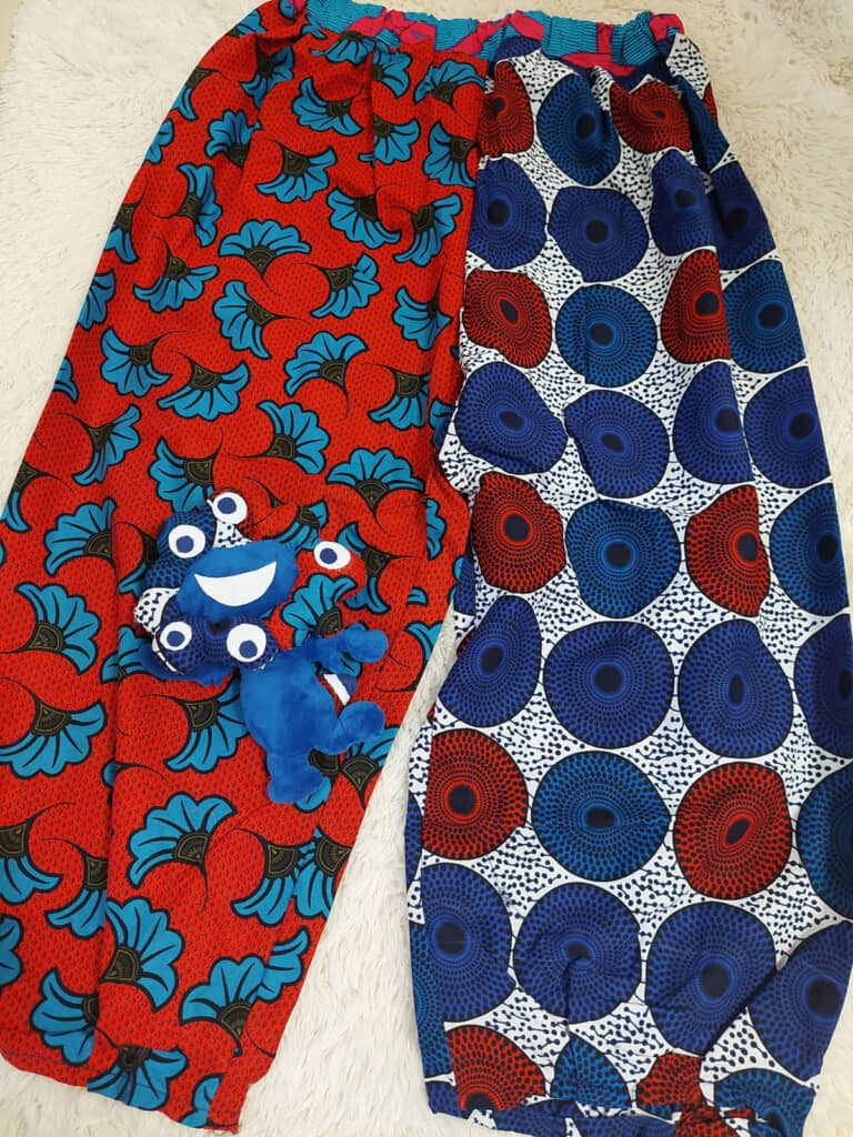 赤地に青い葉柄、白黒に赤青の丸柄の布を半々で縫い合わせたタックパンツ