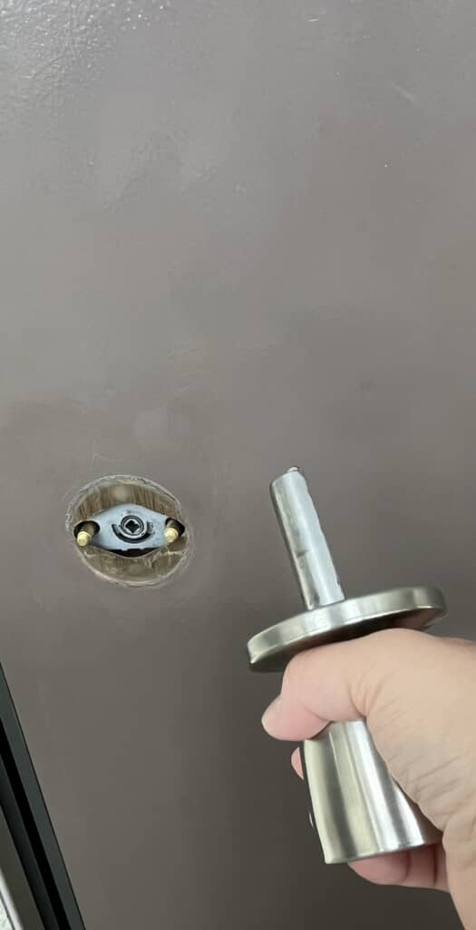 ドアから外れた銀色のドアノブを手に持つ様子、取り付け部分が見えている。