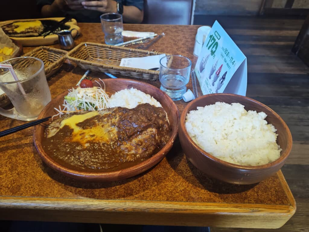 チーズハンバーグカレーとご飯の大盛りセットが木製の器に盛られているレストランの食事。