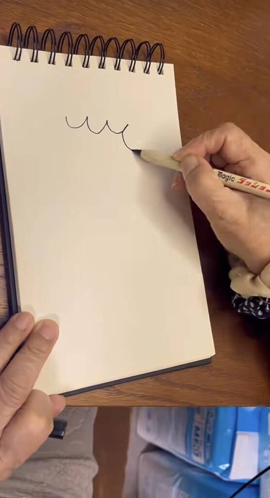 白いスケッチブックに波線を描き始める手元。
