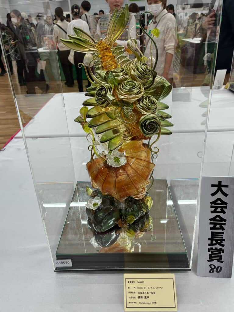 大会会長賞を受賞した飴細工の展示作品で、ガラスケース内に植物や貝殻を模した繊細な造形が並ぶ。