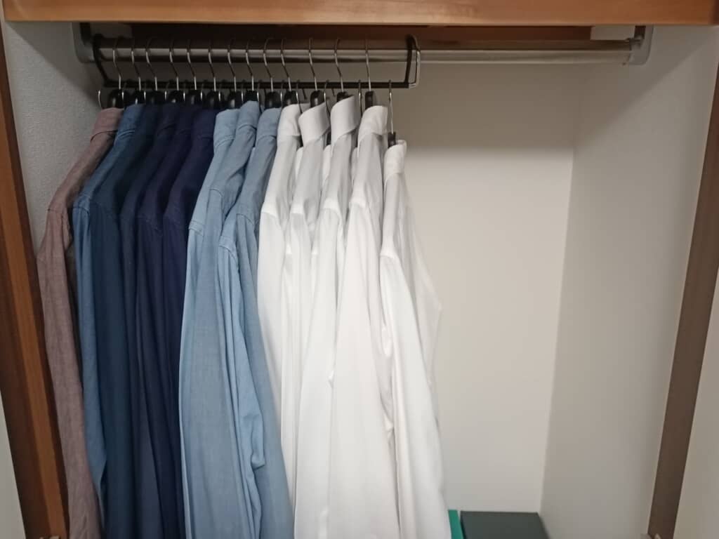 クローゼットに整然と並べられたシャツ。濃い色から白へのグラデーションで配色されている。