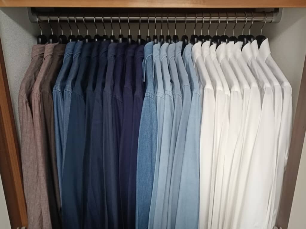 クローゼットに色別に並べられた長袖シャツのコレクション。白から茶色へのグラデーションで整理されている。