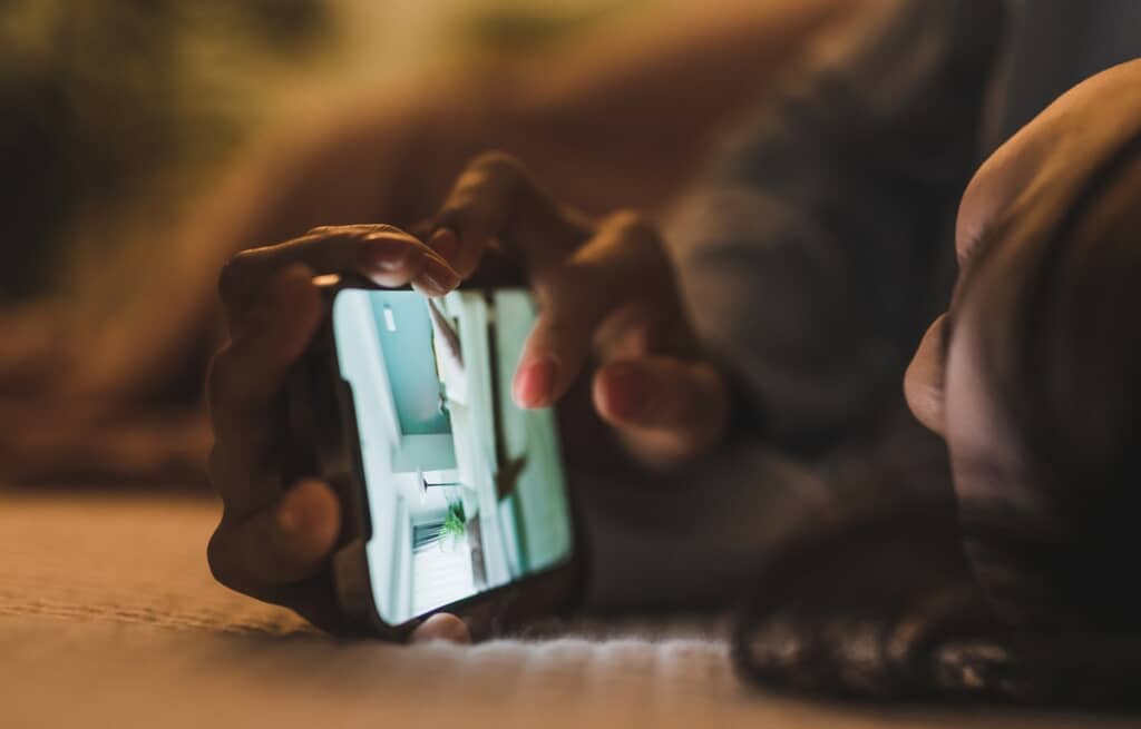 横になってスマートフォンの画面を見る人の写真