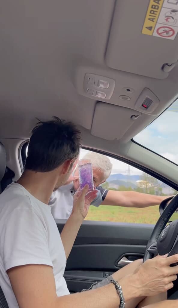 車内の男性が、窓の外から顔を出した年配男性からコップを受け取っている。