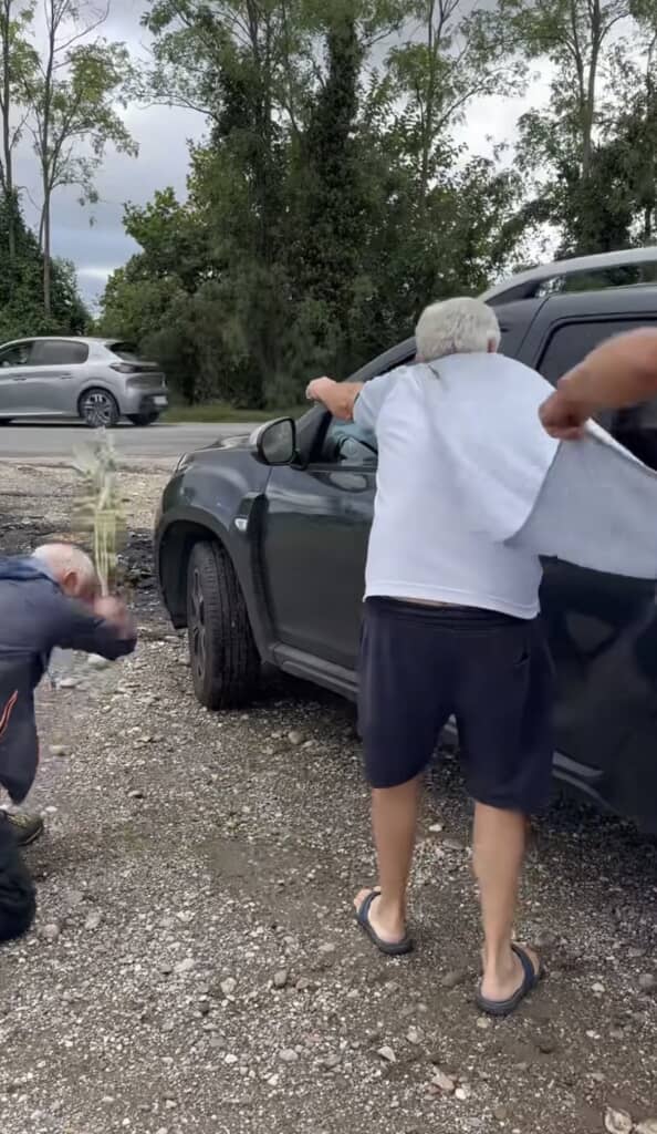 車の外で草を動かす男性と、腕を伸ばしている男性。