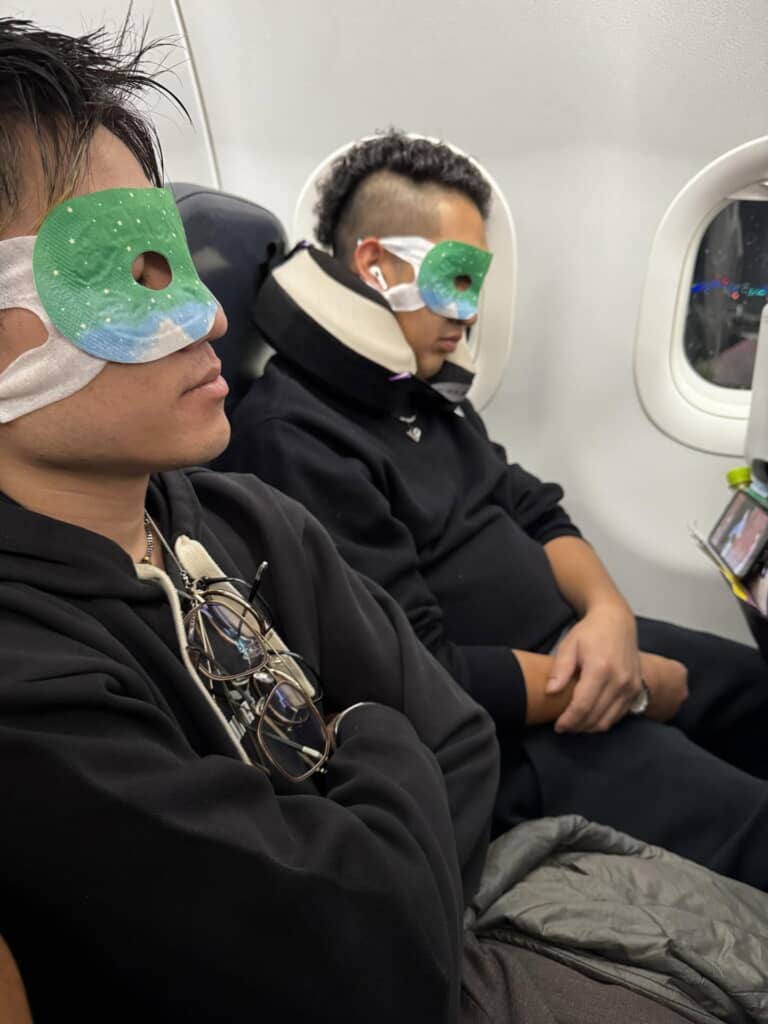 飛行機内でリラックスしながら「ながらほっとアイマスク」を着用して眠る2人の男性。