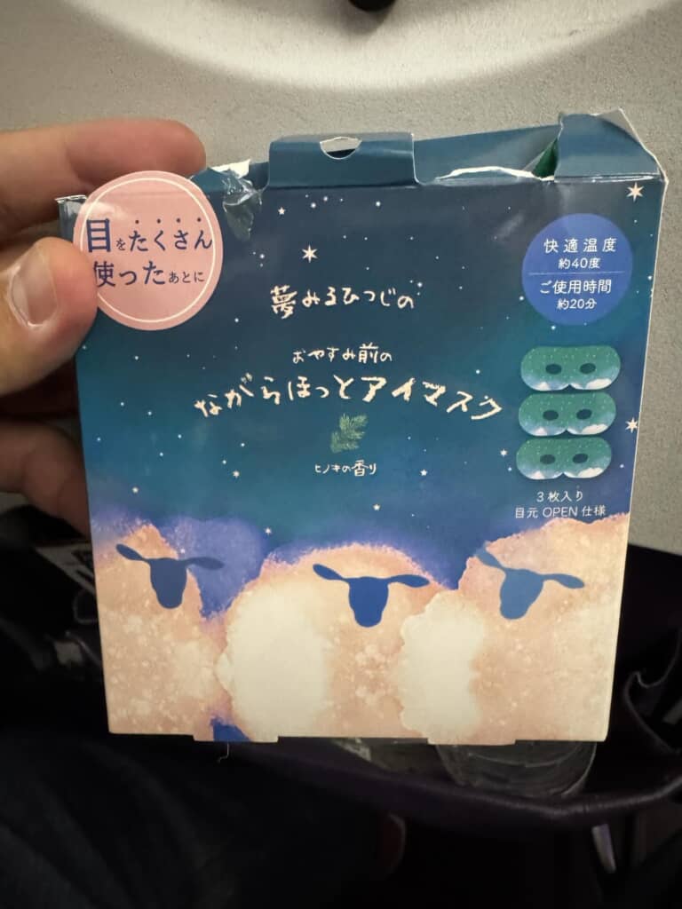 「夢みるひつじのながらほっとアイマスク」のパッケージを手に持った様子。使用時間や香りなどが記載されている。