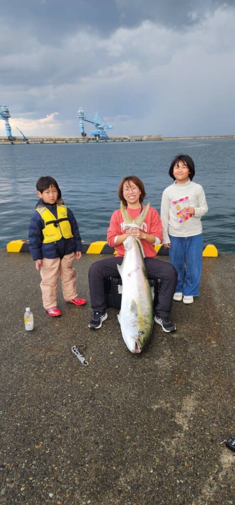 自分が釣り上げた巨大ヒラマサの尾を持って、子どもたちと一緒に記念撮影する妻
