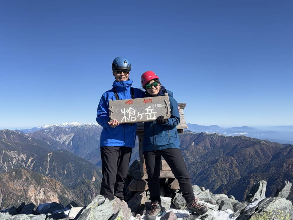 槍ヶ岳山頂で標高3180mの看板を持って笑顔を見せる登山服姿のカップル