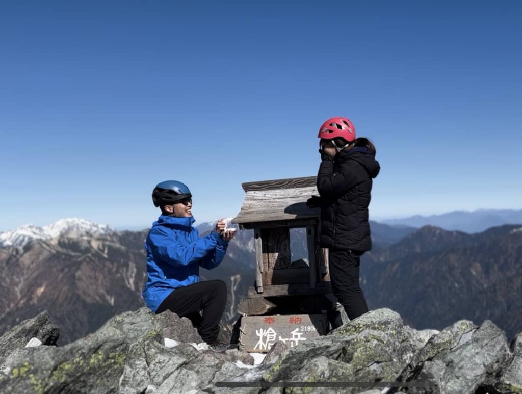 槍ヶ岳山頂の祠の前でプロポーズする登山者と、驚く相手の姿