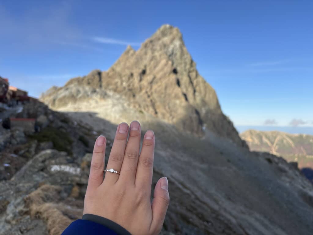 登山者の手に光る婚約指輪と、背景にそびえる槍ヶ岳の鋭峰