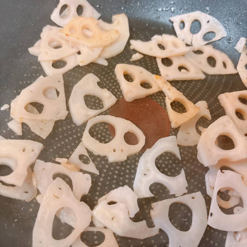 フライパンで炒められている薄切りレンコンの下ごしらえの様子