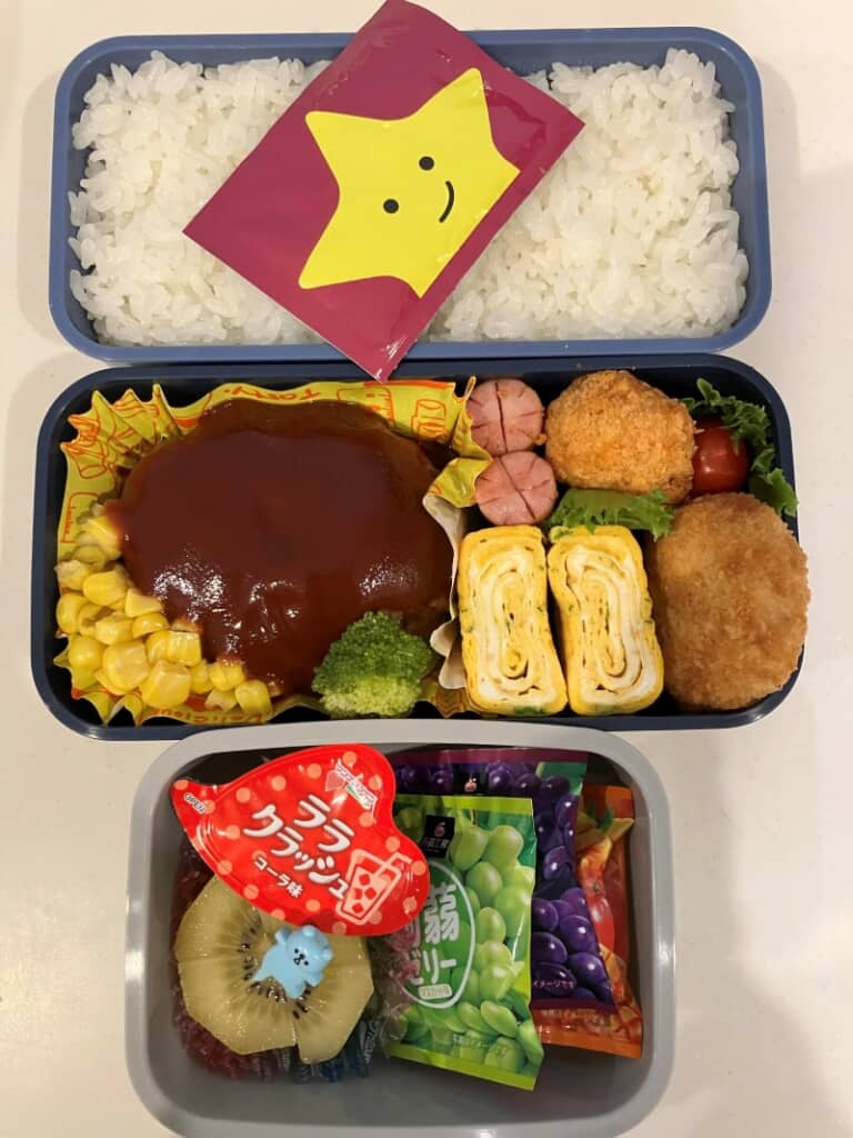 大きなハンバーグと卵焼き、冷凍食品のおかずが詰まっています