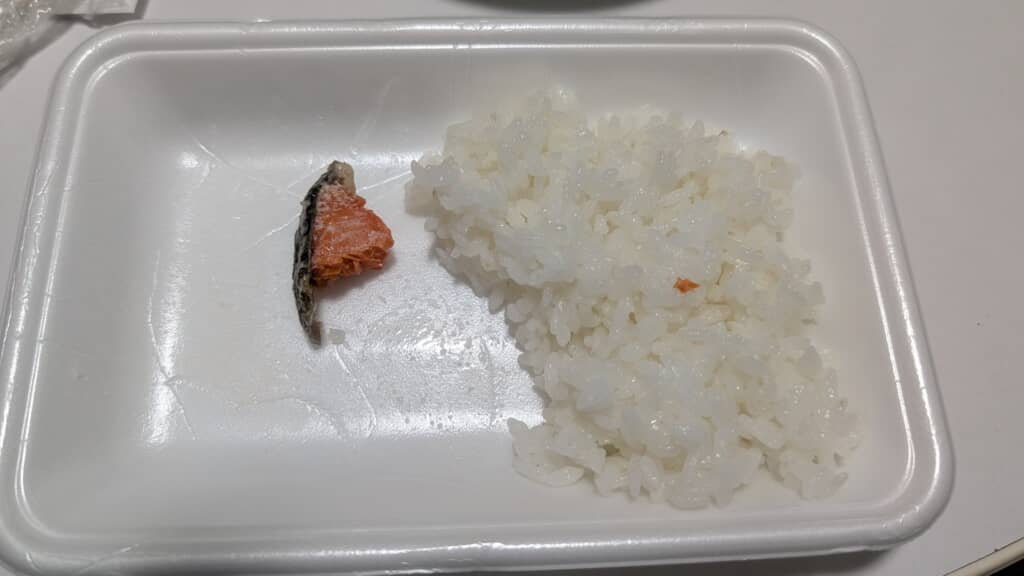発泡トレイに白飯と小さな鮭の切れ端が盛られたシンプルな弁当