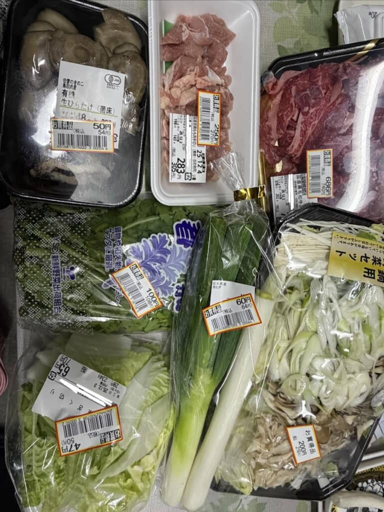 夫が買い物してきた商品を並べている。“お買得品”の値引きシールが貼られた肉や野菜などの食材がずらり