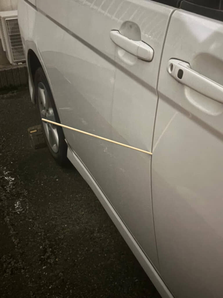 車のドアの隙間に棒編みの棒が挟まっている写真