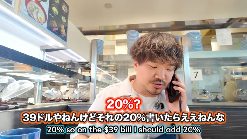 回転寿司店の店内で、男性が電話をしながら会計について話している様子。