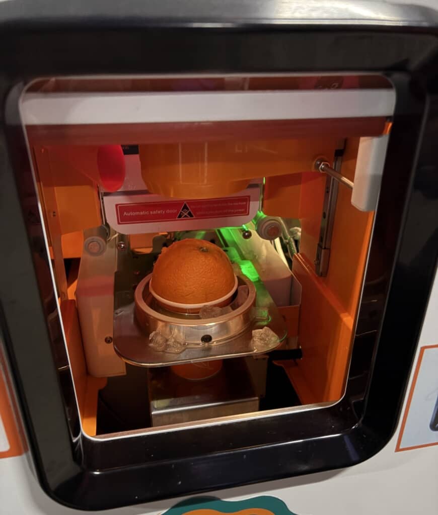 自動販売機から出てきたカップに丸ごとのオレンジが入っている様子