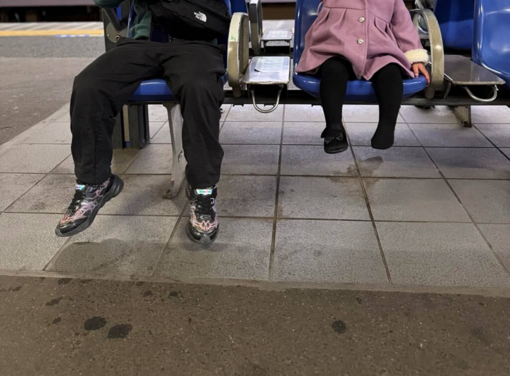 足をぶらぶらさせてベンチで電車を待つ兄妹