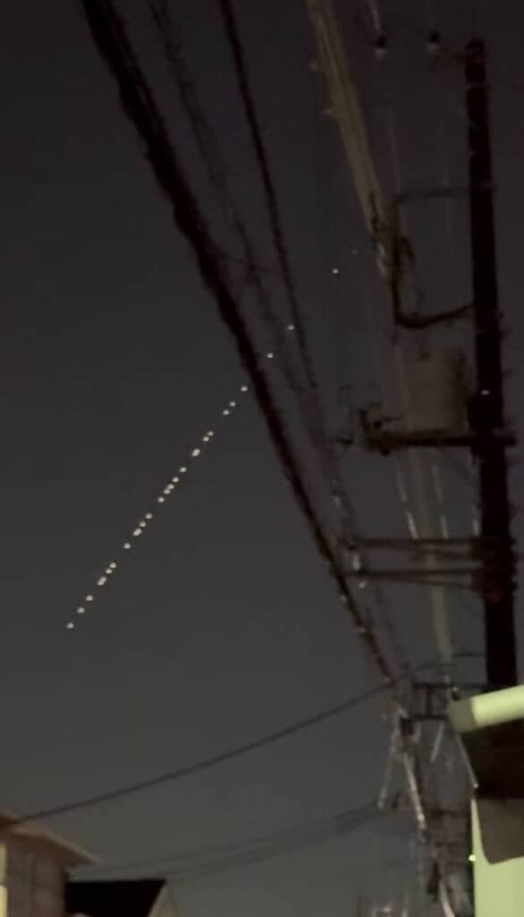 夜の空を斜めに並ぶ小さな光と電柱の風景