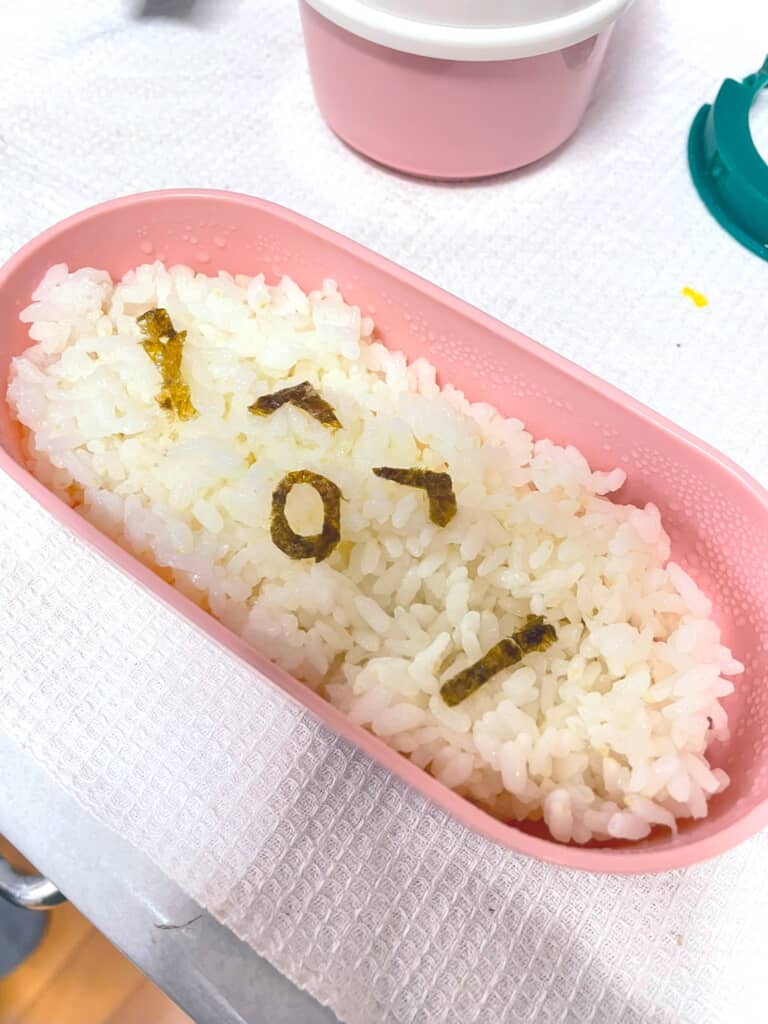 ピンクの弁当箱に入った海苔文字の白ごはん